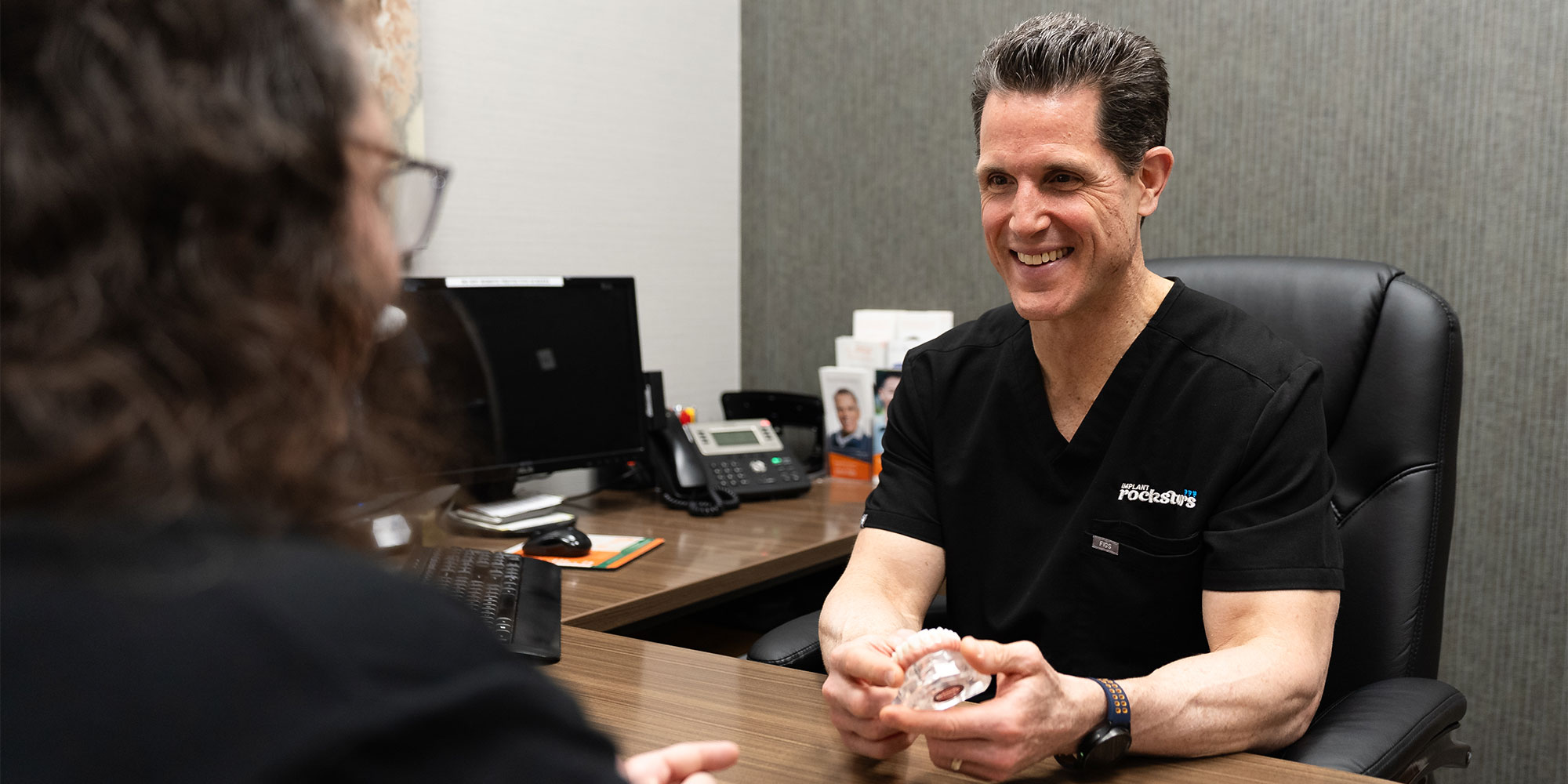 doctor holding dental implant model consulting with patient