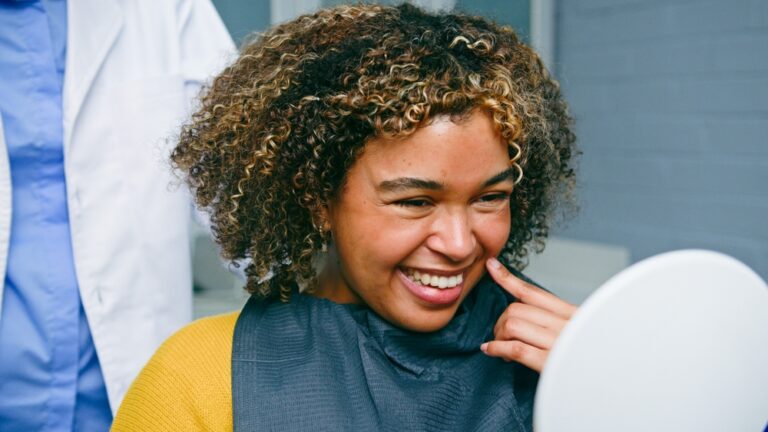 Smiling woman talking with a friendly dentist in a modern office setting. The dentist is pointing to digital x-rays on a screen. No text on image.