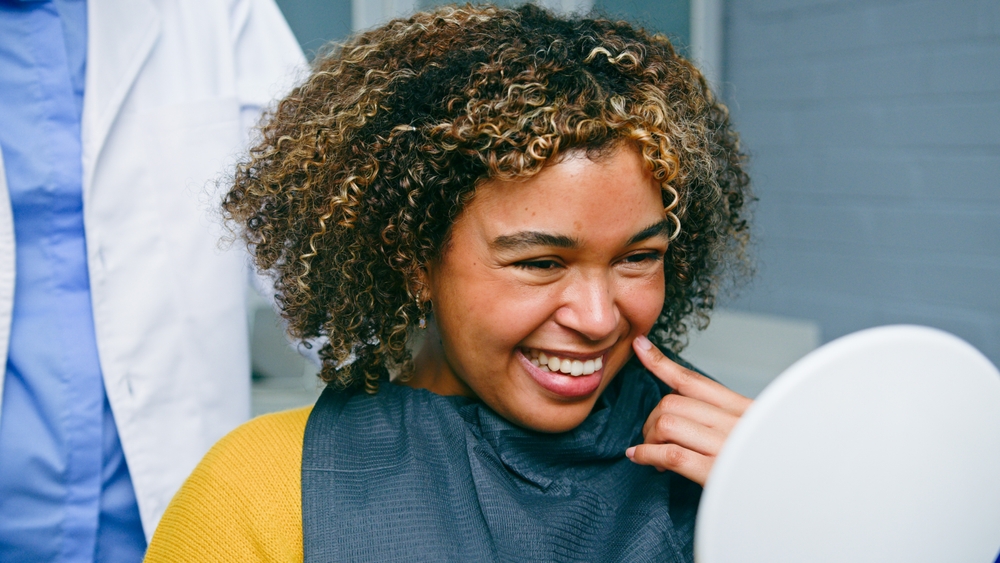 Smiling woman talking with a friendly dentist in a modern office setting. The dentist is pointing to digital x-rays on a screen. No text on image.