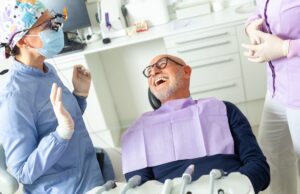 A smiling dentist is shown gently examining a young child's teeth. The child looks relaxed and comfortable in the dental chair with the parent in the background. No text on the image.